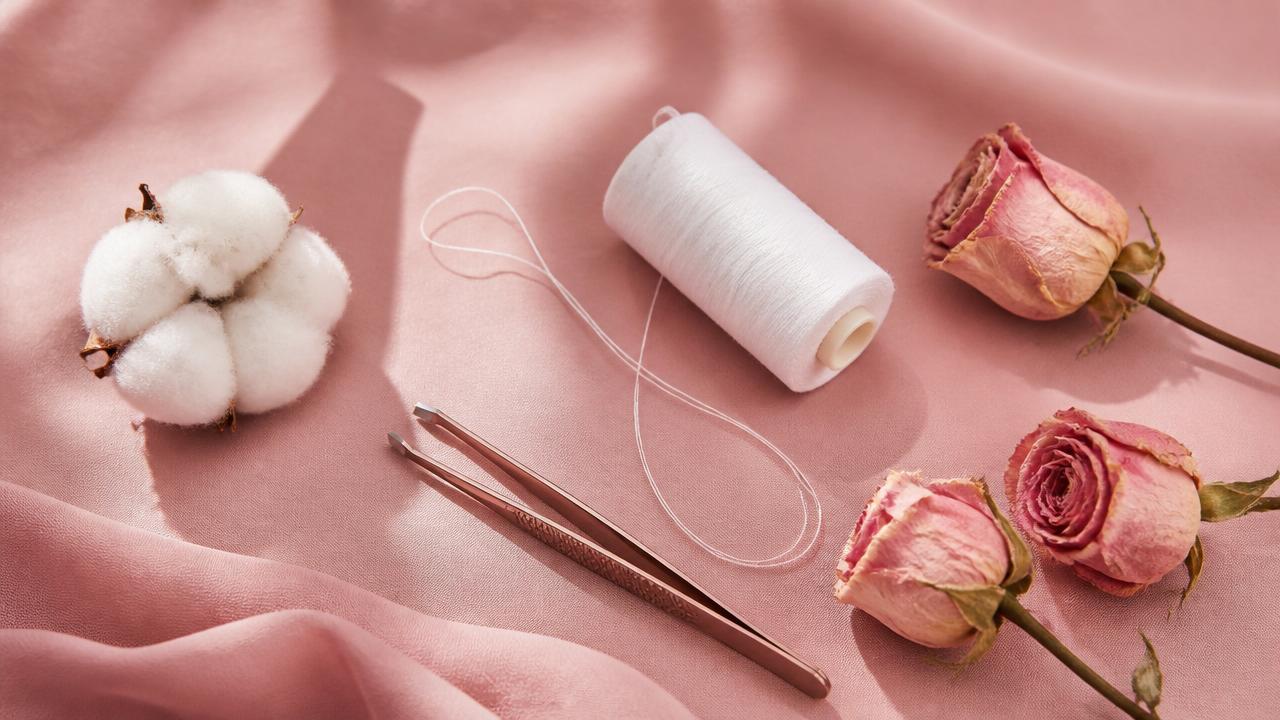 Bobine de fil de coton, pince à épiler et roses sur fond rose poudré — efficacité de l'épilation au fil